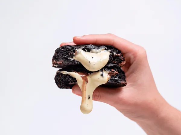 Cookie Trio Chocolat partido ao meio: massa preta com recheio de chocolate branco escorrendo