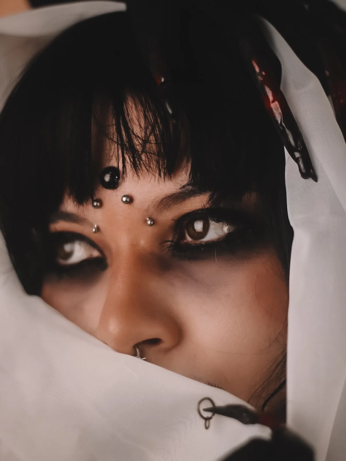 Modelo com piercings olhos de aranha na testa, em ensaio escuro