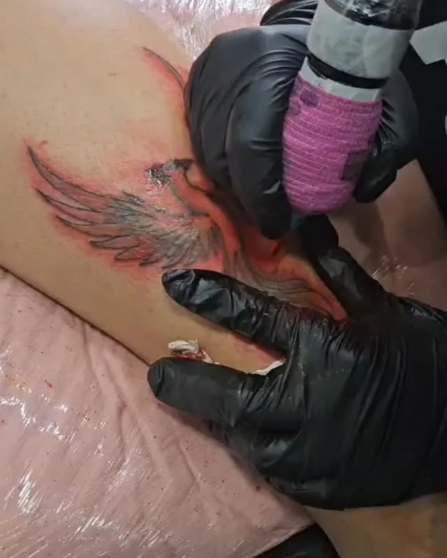 Diva tatuando, de luvas pretas, com a máquina na mão