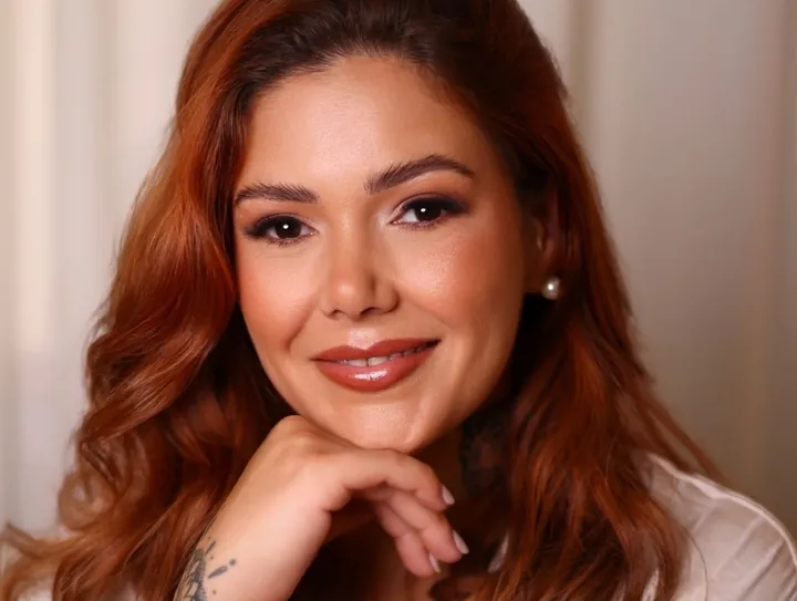 Retrato da Fabi Gomez, de cabelo ruivo, a sorrir com a mão no queixo