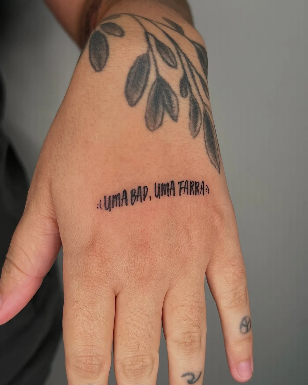 Ramo de folhas na mão e frase no punho