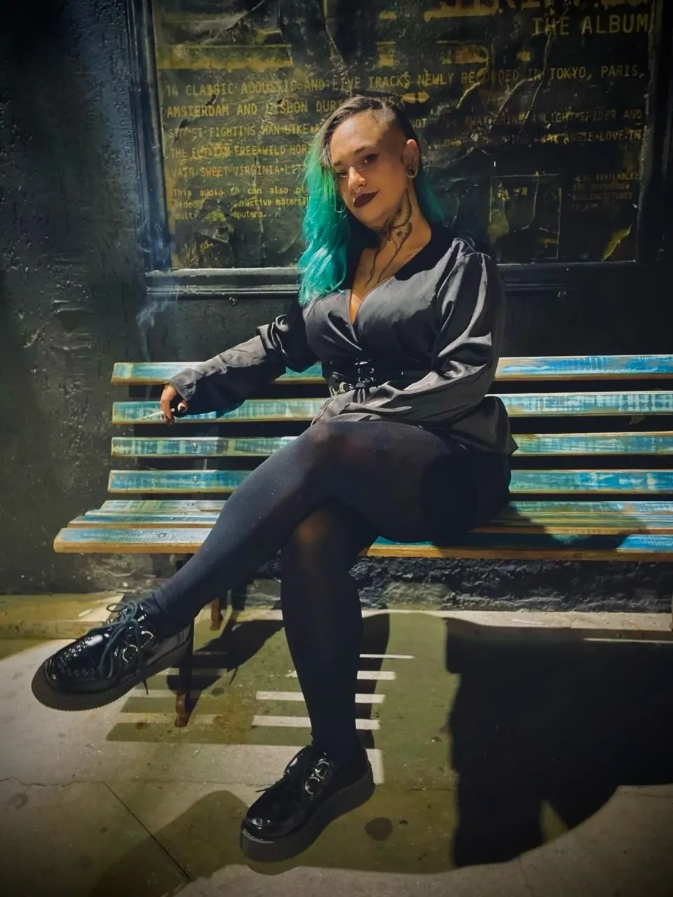 Bárbara Gomes, de cabelo azul, sentada num banco de praça à noite
